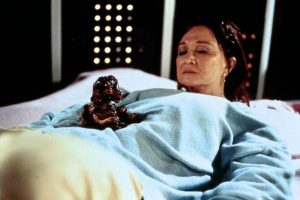 Diane Ladd looking dolefully at a bloody dinosaur emerging from her uterus.